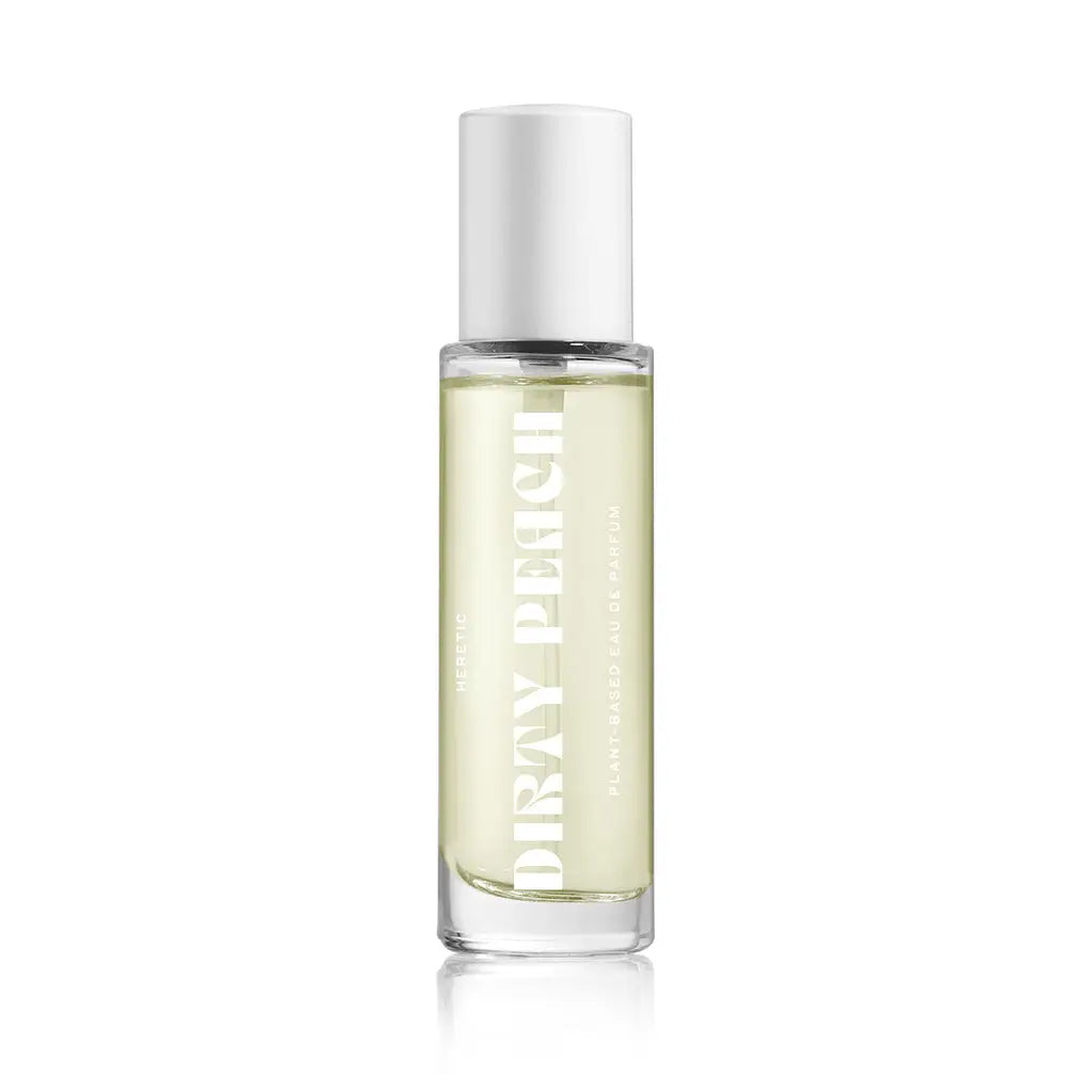 A clear glass Heretic 15ML Perfume bottle by Faire, featuring a white cap and light yellow liquid. The "DIRTY PEACH" label suggests a plant-based fragrance with sandalwood and vanilla notes.