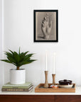 Above a wooden cabinet hangs the Dreyer Hand Drawn After Plaster by Faire, framed and printed on matte art paper. The cabinet features a potted plant, books, and a wooden tray with candles, bowl, and small dishes for displaying art.