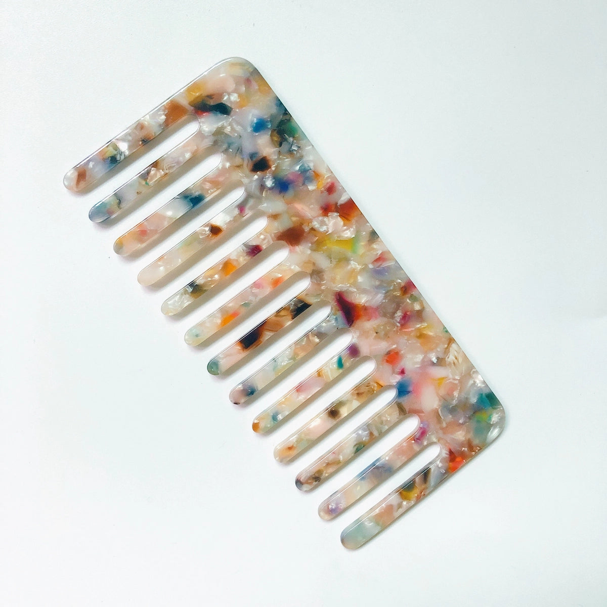 The Faire Hair Comb Assorted is a wide-tooth, anti-static comb made of translucent material with a vibrant marbled pattern in orange, blue, pink, and white, shown on a plain white background.