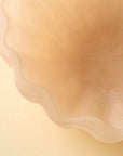 Close-up of the Indaba Scallop Resin Bowl, featuring pale, wavy edges and an opalescent finish. Its smooth texture and soft, curved lines are showcased against a light beige background.