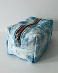 The Faire Dyed Toiletries Bag is a rectangular, hand-dyed blue and white cotton pouch with a metal zipper and red trim, shown on a light surface—ideal for organizing your desk.