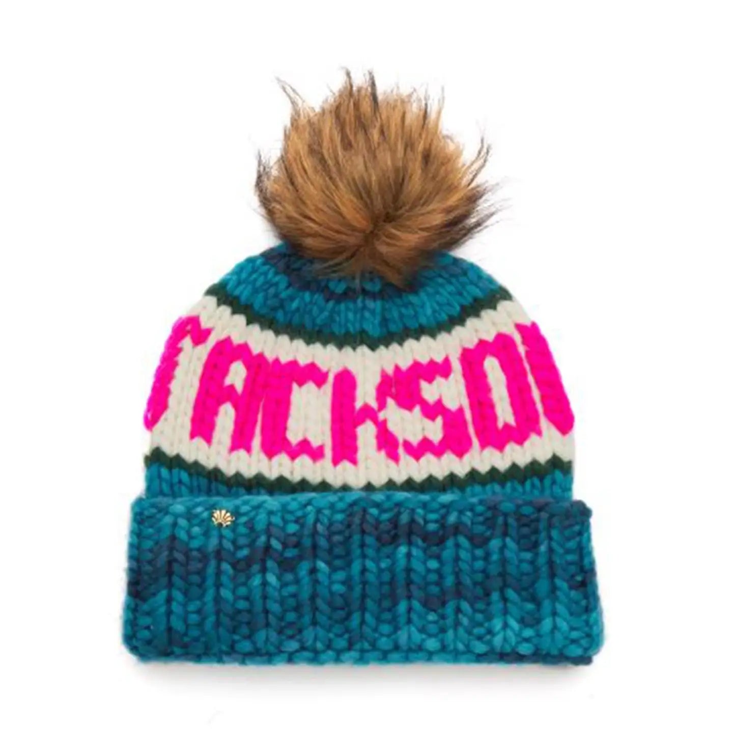 The Faire Knit Ski Hat is a luxury blue, teal, and white merino wool beanie featuring a large brown faux fur pom-pom and bold pink "JACKSON" lettering across the front.