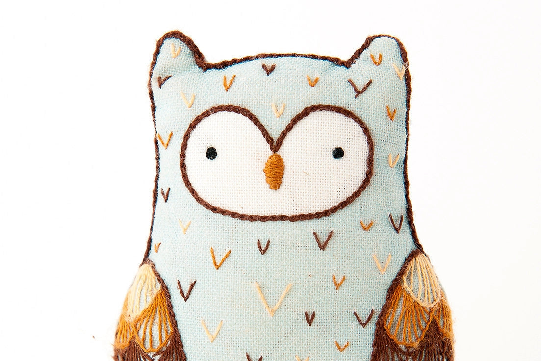The Horned Owl Embroidery Kit by Faire features a charming horned owl design with light blue fabric, embroidered eyes, and brown and beige wing details, perfect for crafting your own soft handmade plush.