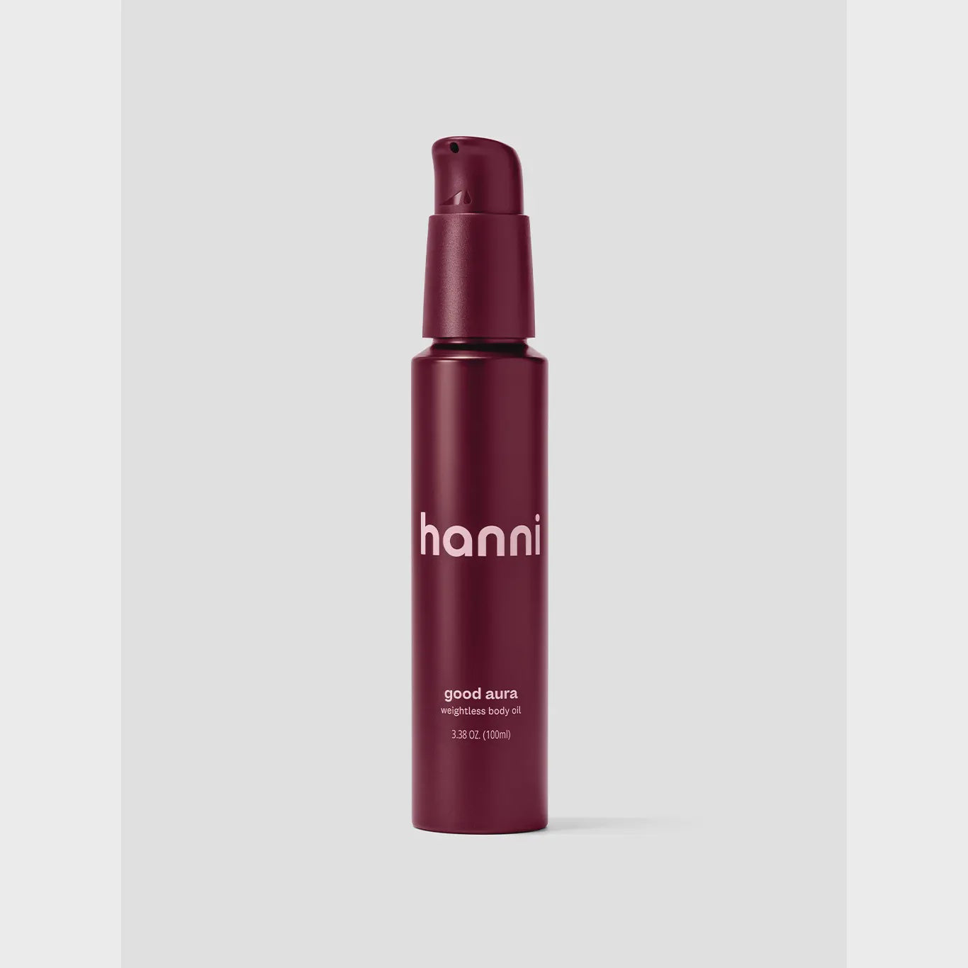 A maroon cylindrical bottle of Hanni Good Aura weighted body oil by Faire, featuring a pump dispenser, is set against a light gray background. It promises nourishment without greasiness and showcases white text.