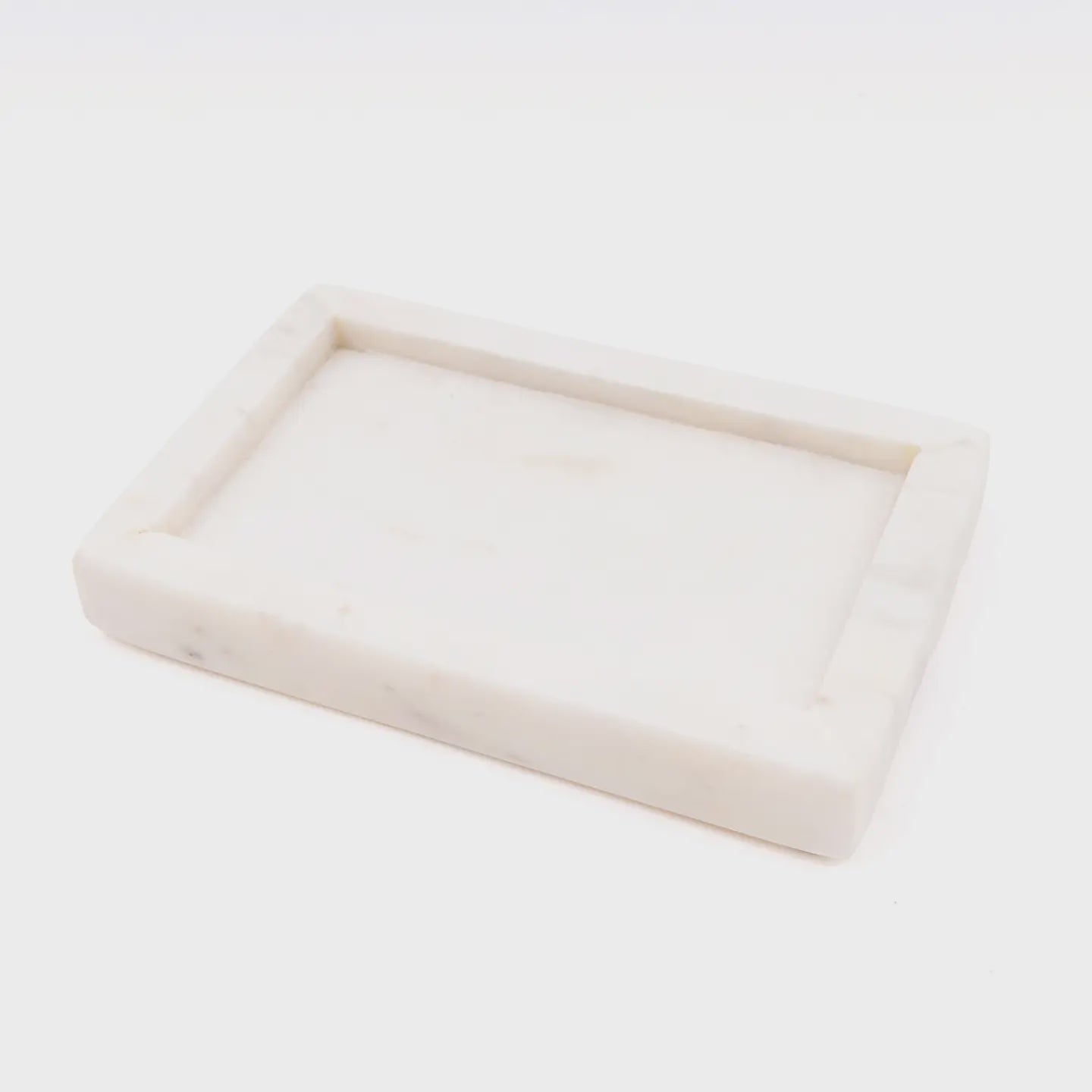 A beautiful rectangular White Marble Soap Dish by Faire, featuring raised edges and a smooth finish, is elegantly displayed on a plain white background. This handcrafted piece is perfect for both decorative and serving purposes.