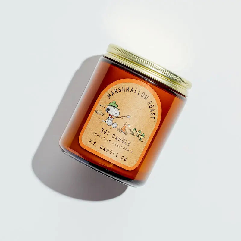 The brown jar candle with a gold lid, labeled "Marshmallow Roast" and depicting a marshmallow on a stick, is crafted by Faire. This soy wax candle in its amber jar uses fine fragrance oils for ambiance. Originally by PFC Candle Limited.