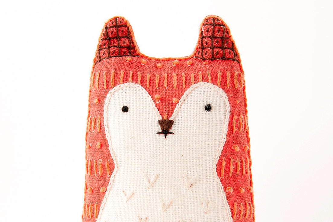 The Faire Fox Embroidery Kit lets you craft a handmade plush fox with screen printed fabric, featuring a red-orange body, white face and chest, black stitched nose and eyes, plus textured embroidery details.