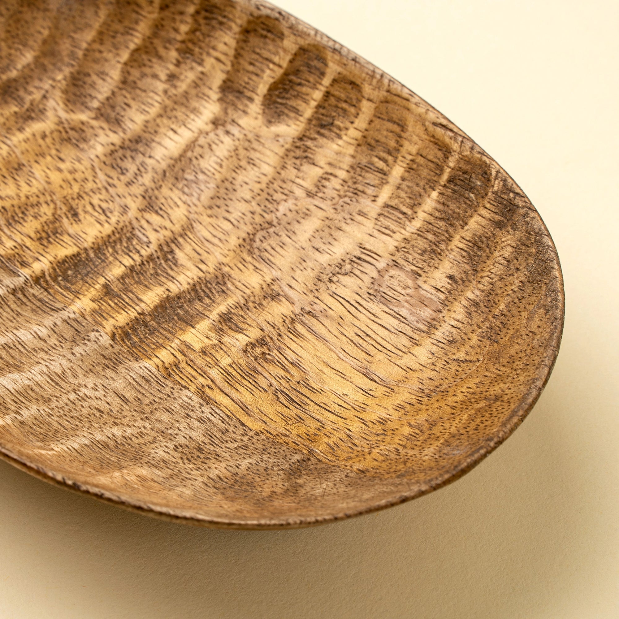 Mango wood Terrain Carved Dish S by Faire with striped grain, shown on a beige background.