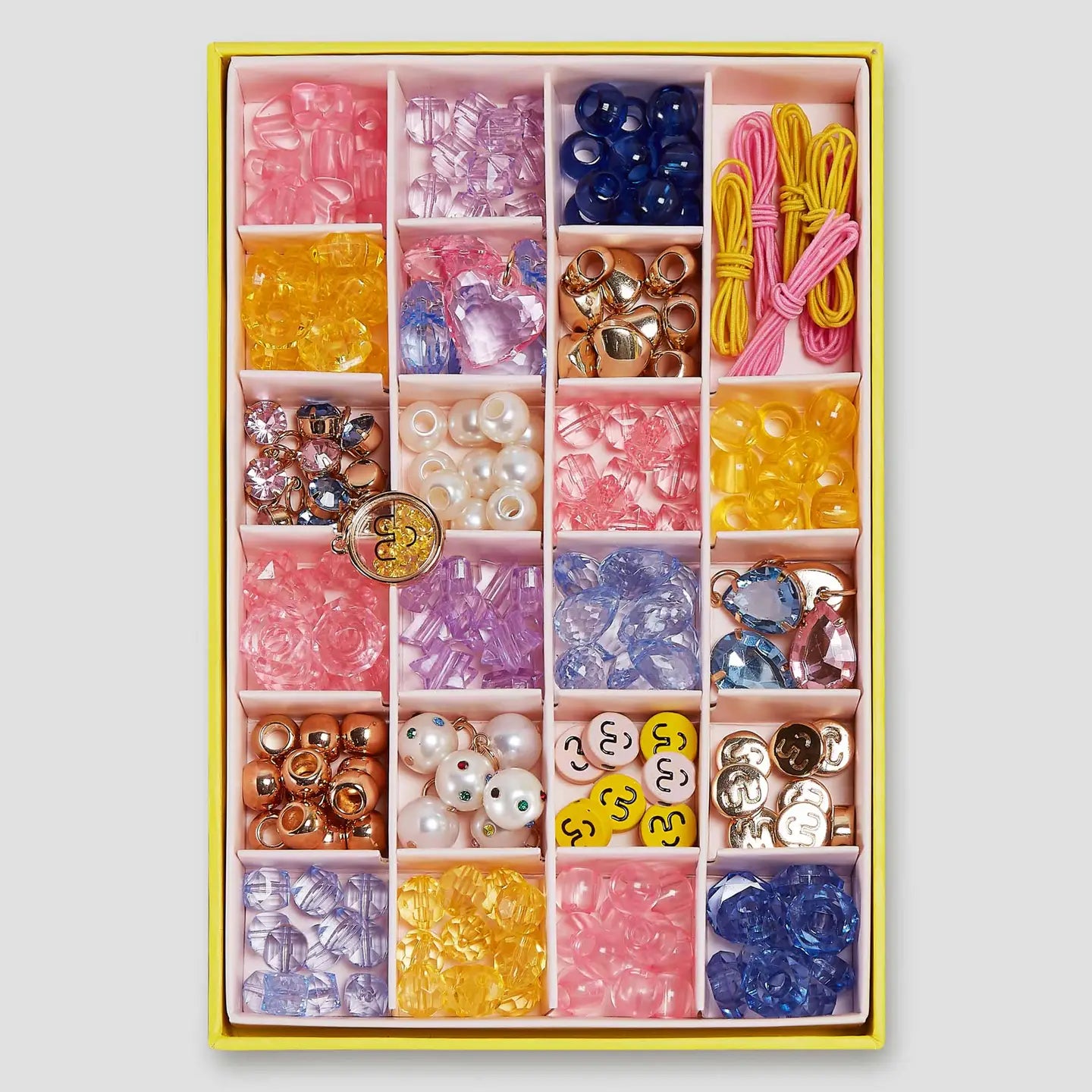 The Faire Make It Super DIY Bead Kit includes a neatly organized box of colorful beads in various shapes and colors like pink, yellow, blue, and clear. It features compartments for easy access and comes with smiley face beads and strings.