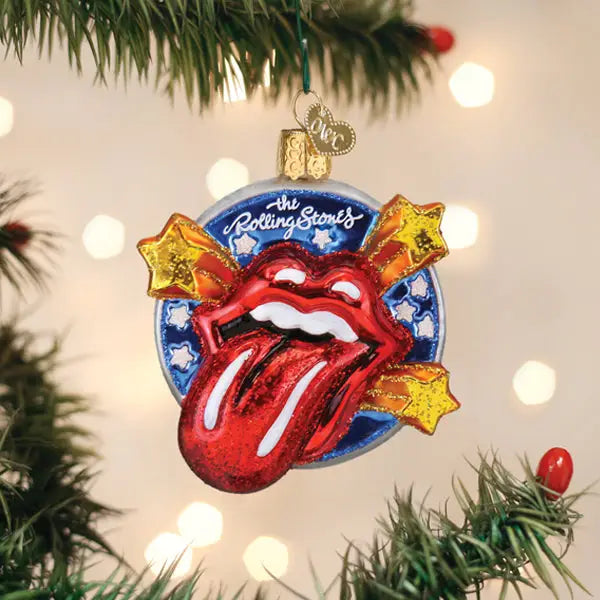 An Old World Ornaments piece by Faire hangs on a tree, displaying the Rolling Stones’ iconic red tongue logo with shooting stars and white-starred blue background, adding to a festive assortment of ornaments.