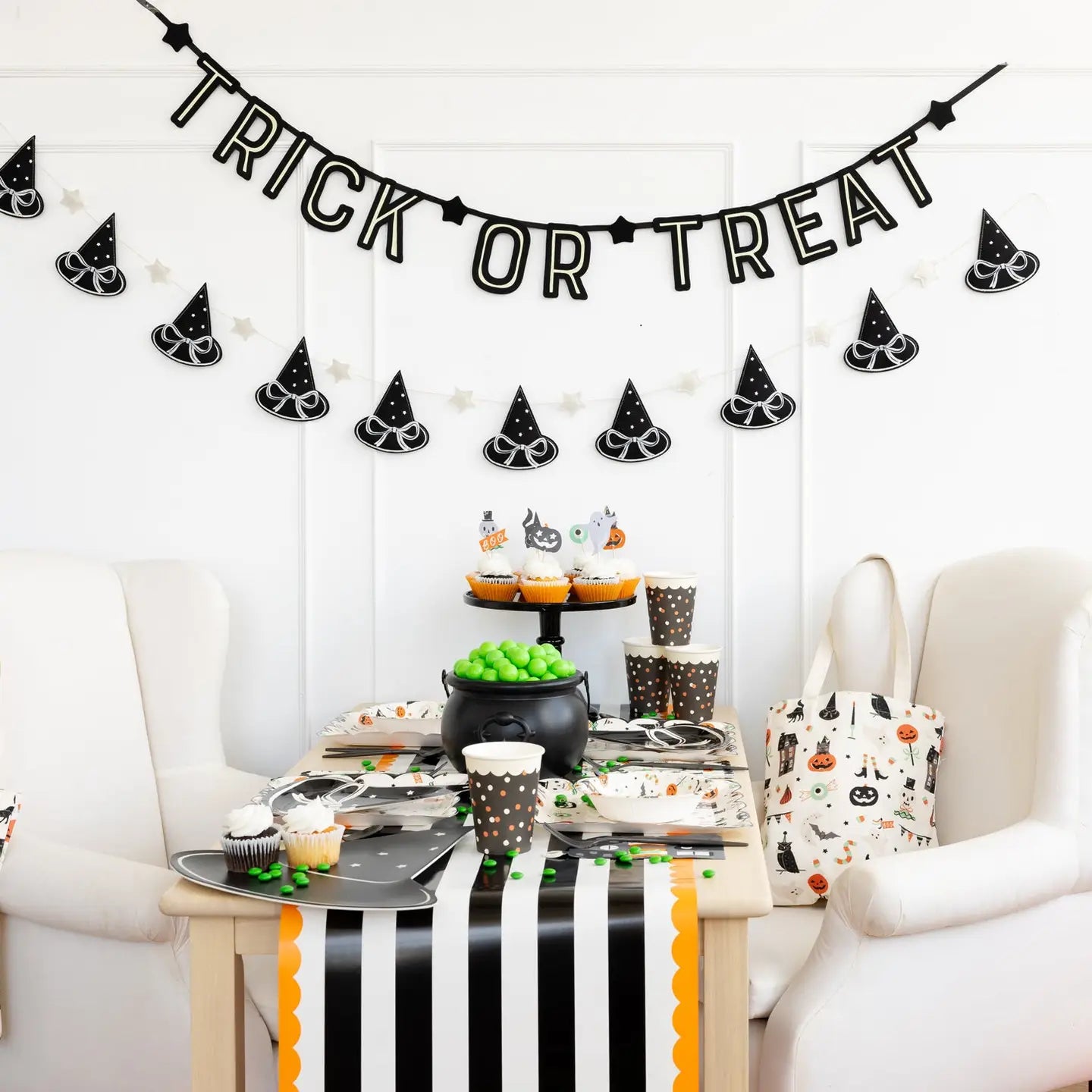 A Halloween table setup features black and white decor, cupcakes, party hats, a cauldron with green candy, a striped table runner, and the My Mind's Eye Bunting Banner glowing above.