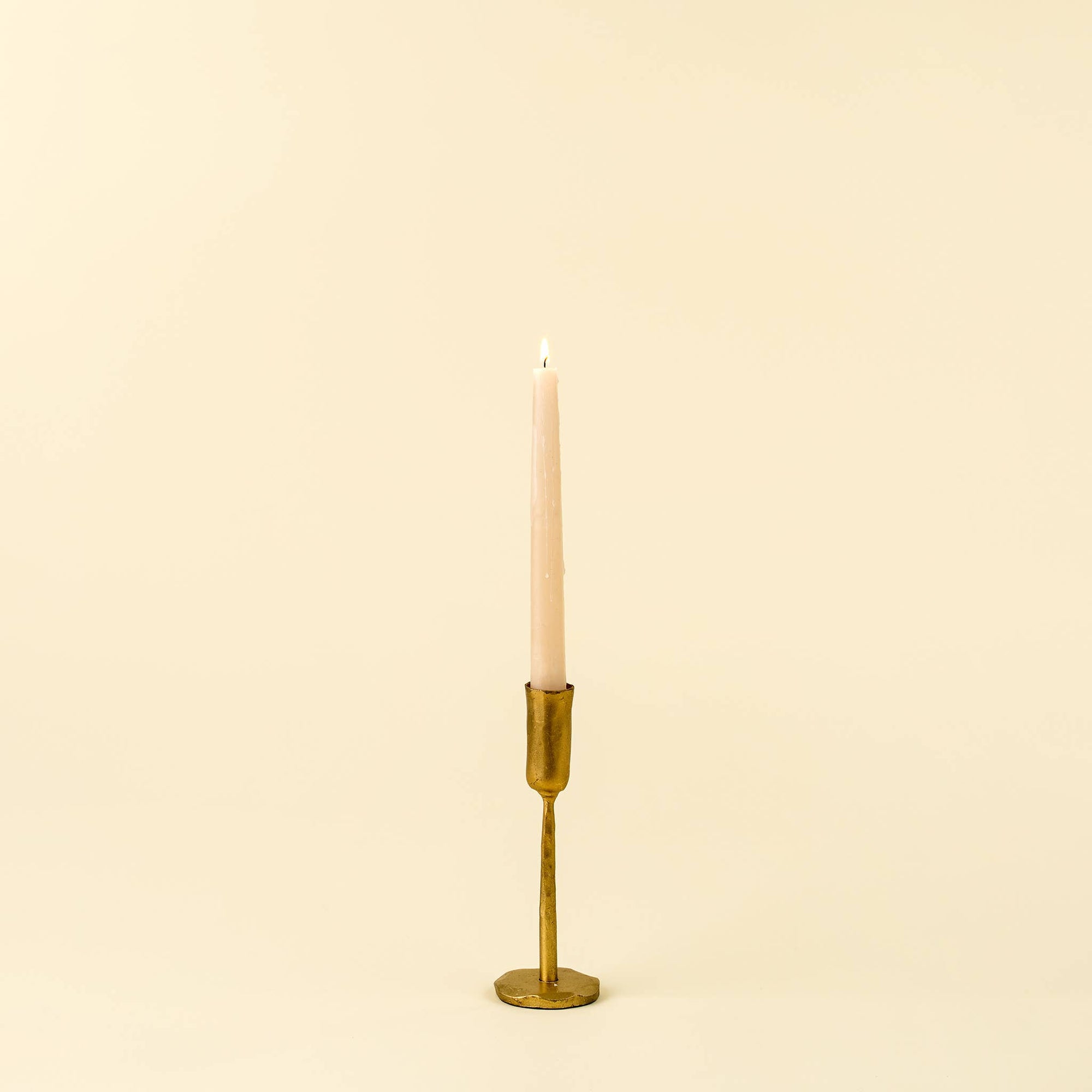 Gold Faire Luna Forged Candlestick S holding a pink taper candle, shown against a neutral beige background.