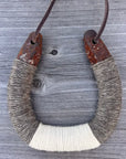 The Faire Lucky Horseshoe features upcycled metal wrapped in gray and white yarn, hanging by a leather cord against a weathered wood background—a perfect rustic decor piece.