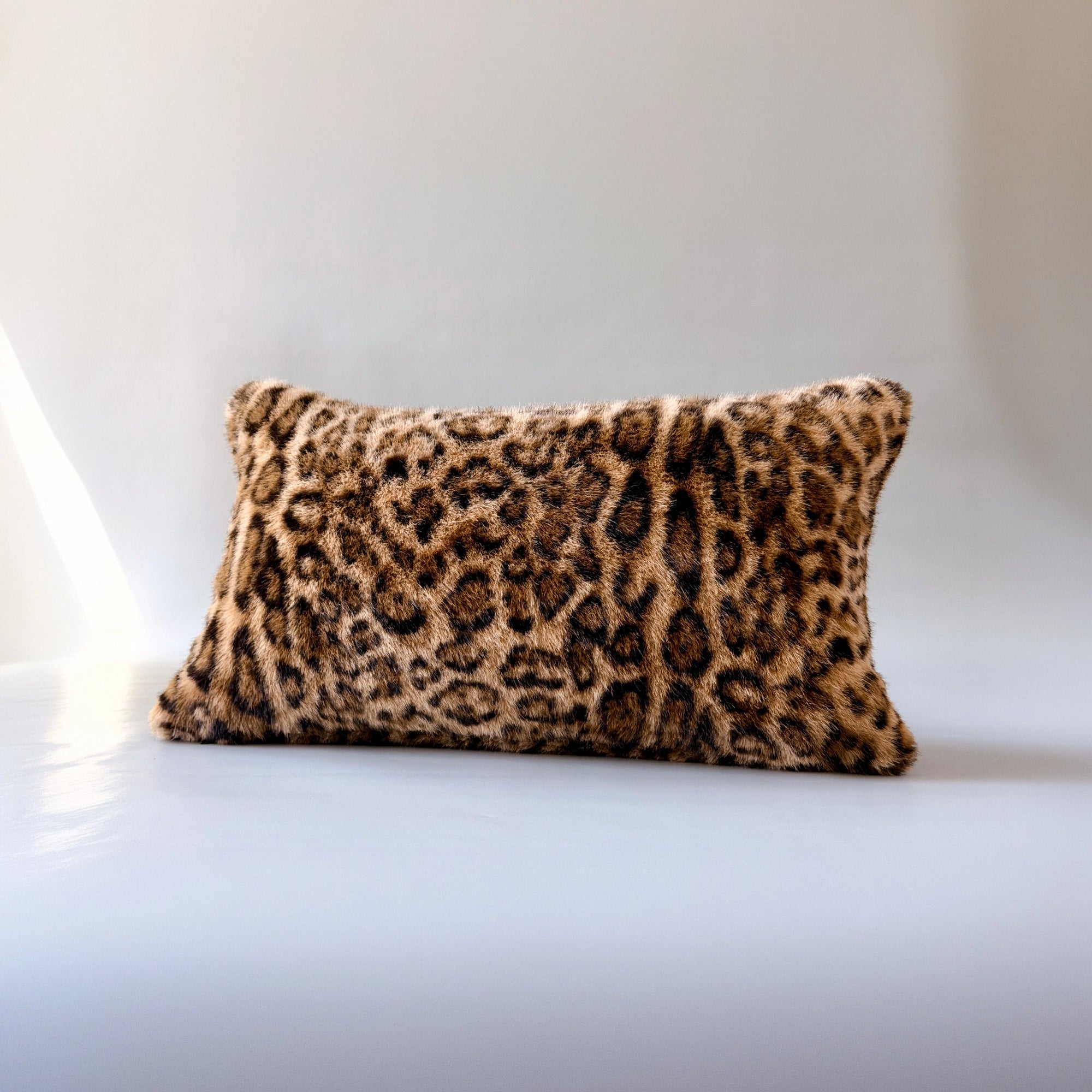 Leopard print lumbar pillow with plush faux fur cover by Faire, shown on a sleek white surface.