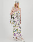A woman stands against a white background wearing the Me369 Olivia Camisole Dress featuring a colorful Enlightenment pattern, with a matching headscarf, white shoes, and a large coordinated shoulder bag.