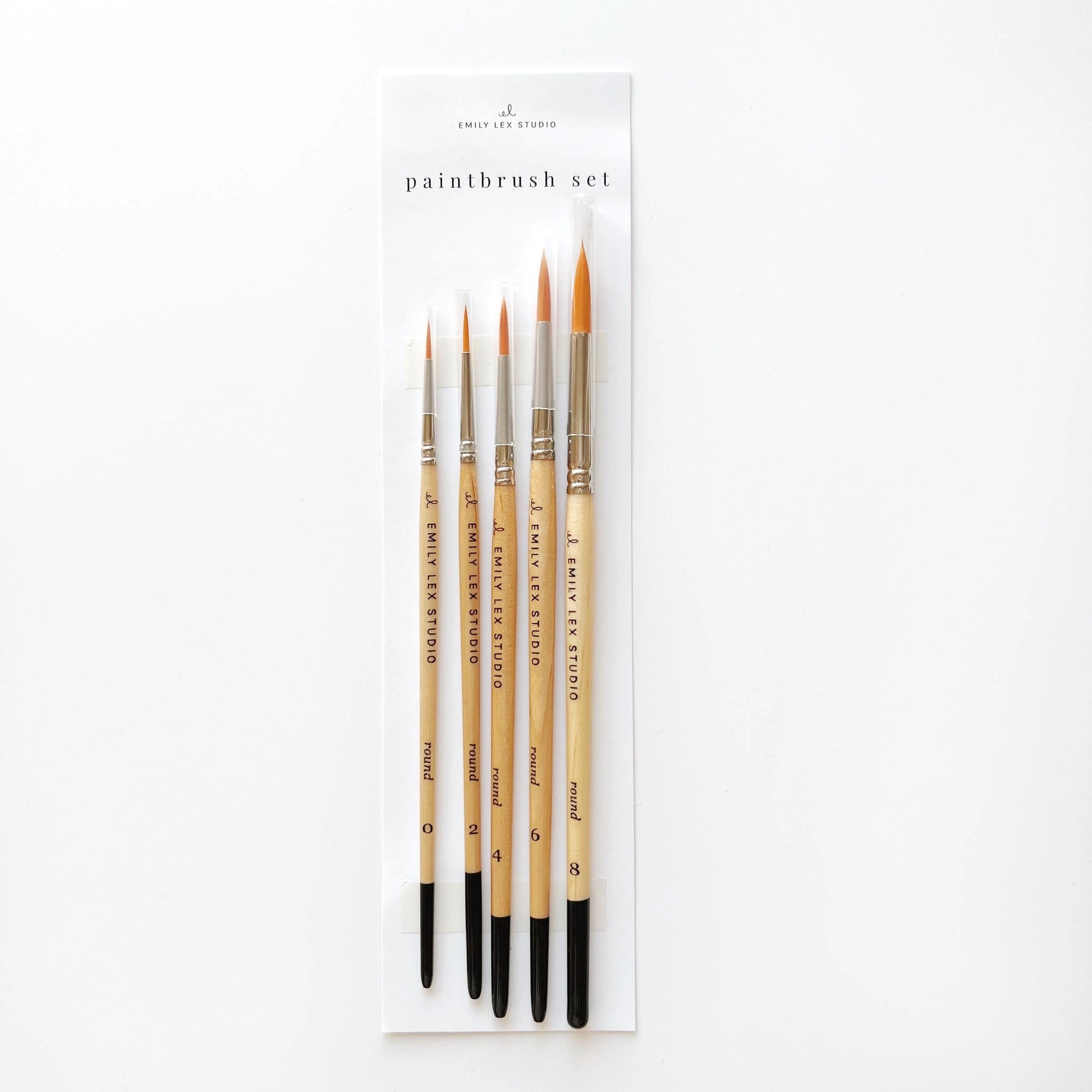 The Faire Paintbrush Set includes five wooden-handled brushes with fine synthetic Taklon bristles, ideal for watercolor painting, arranged on a white backing card labeled “Paintbrush Set.”.