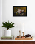 The Faire Van Huysum Flower Still Framed art hangs on a white wall above a shelf with a potted plant, two lit wooden-cased candles, stacked books, and a tray that holds a ceramic dish and small bowls.