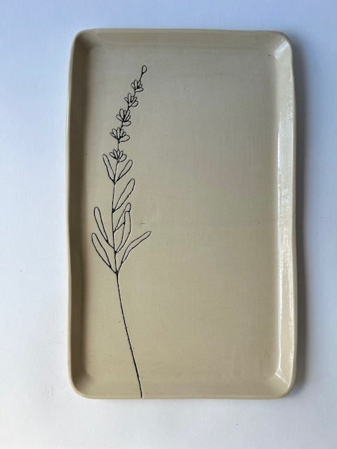 The CSF Tray by Faire is a rectangular beige ceramic plate featuring a simple black line drawing of a lavender sprig on the left, set against a white background for an elegant and calming touch.
