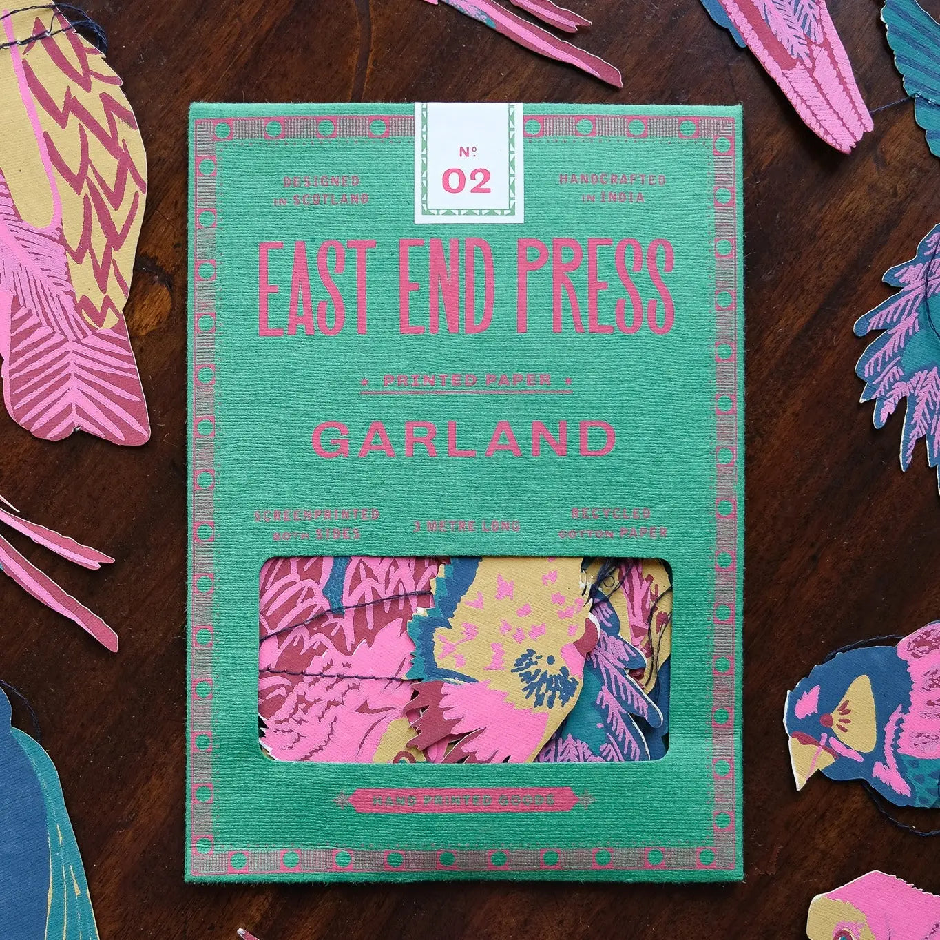A green and pink Faire box with a window displays colorful bird-shaped Paper Garland/Chains inside, surrounded by matching bird cutouts—ideal festive décor for any space.