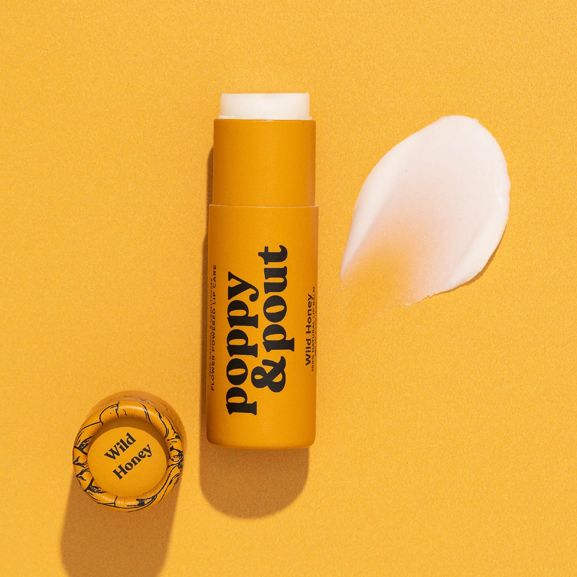 A yellow tube of Faire Poppy & Pout Lip Balm is displayed on a yellow background, its matching cap beside it and a smear of the balm to the right.