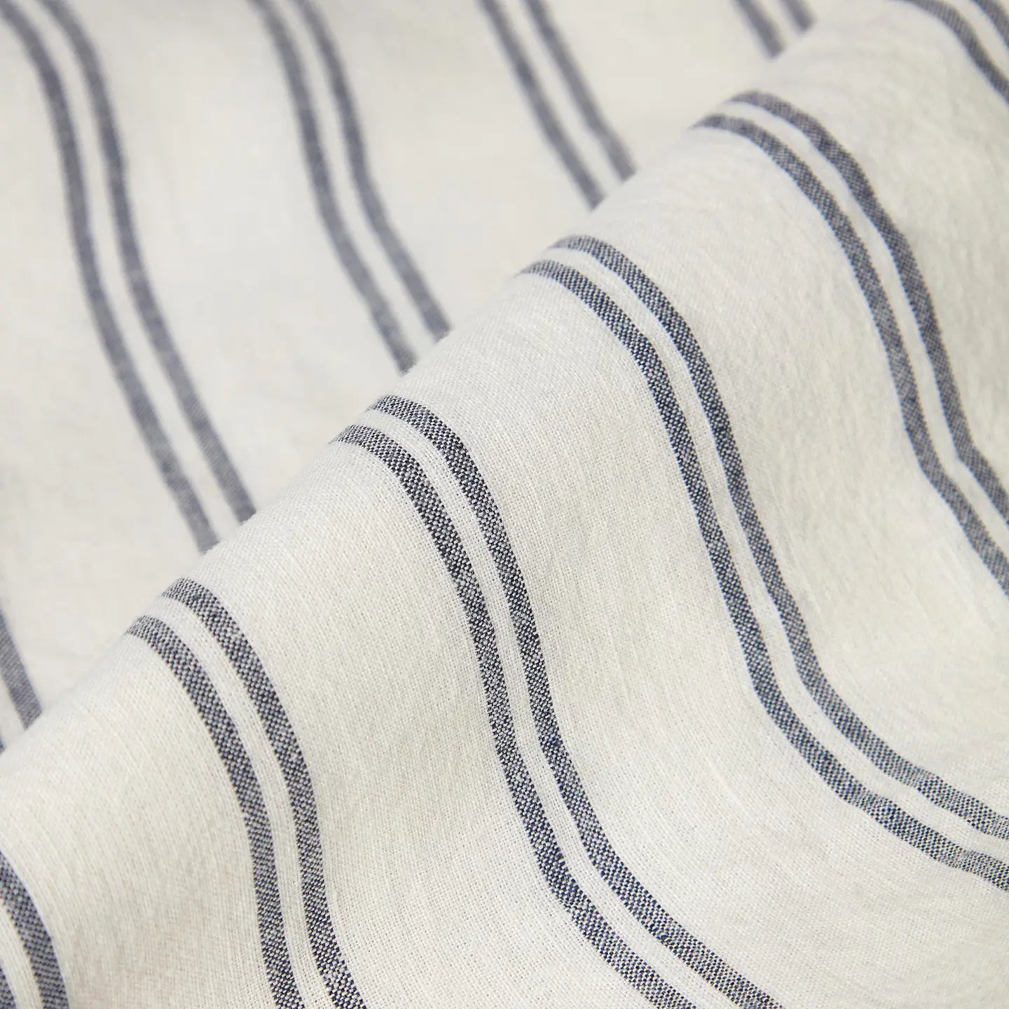 Close-up of the Kemptown Stripe Linen Euro Sham by Faire, featuring off-white European linen with thin, diagonal navy blue stripes. The breathable fabric looks soft, slightly textured, and gently folded.