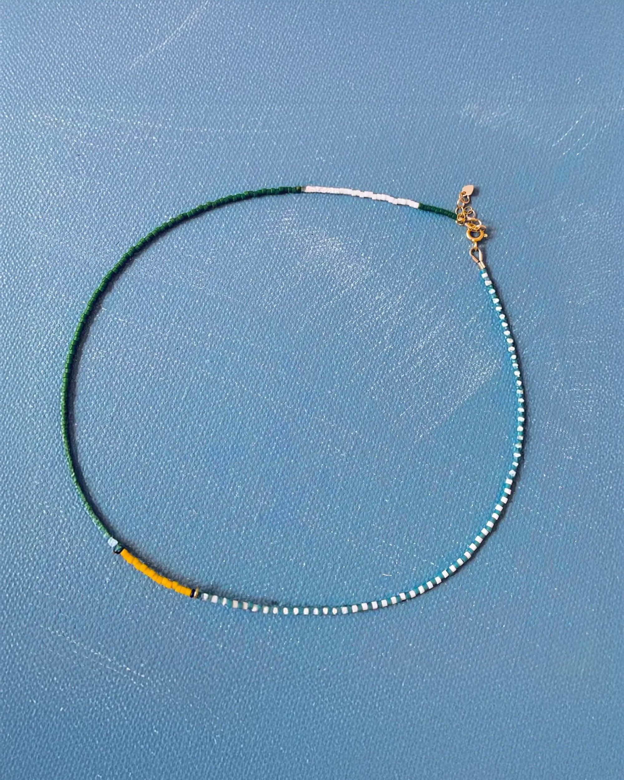 The Faire AR Line Necklace in Fairway Green features small Japanese glass beads in green, white, and yellow sections with a gold-filled clasp.