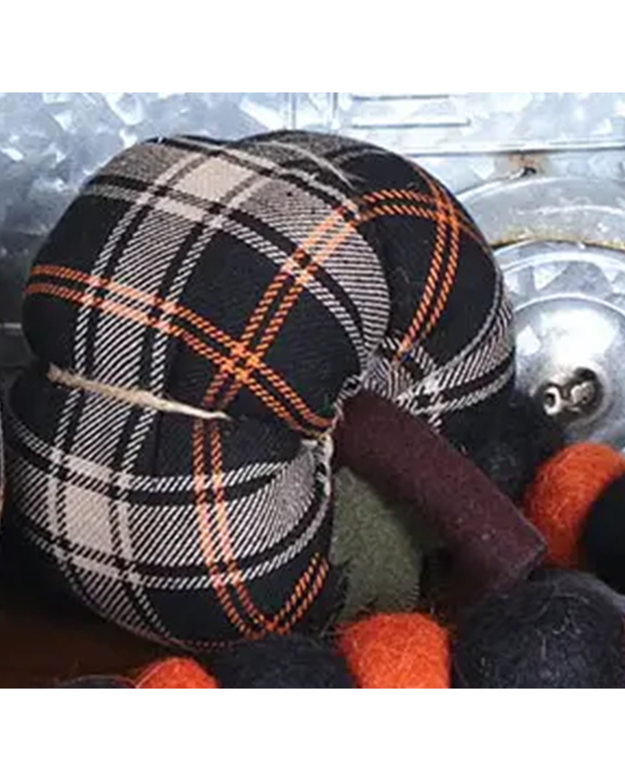 The Pumpkin by Faire is a plaid, pumpkin-shaped autumn ornament in black, white, and orange fabric, accented with matching felted balls—perfect for cozy farmhouse decor on a metallic background.
