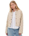 A woman faces the camera with a neutral expression, wearing the Denimist FAULKNER QUILTED JACKET in light beige over a white button-up shirt and blue jeans, set against a plain background.