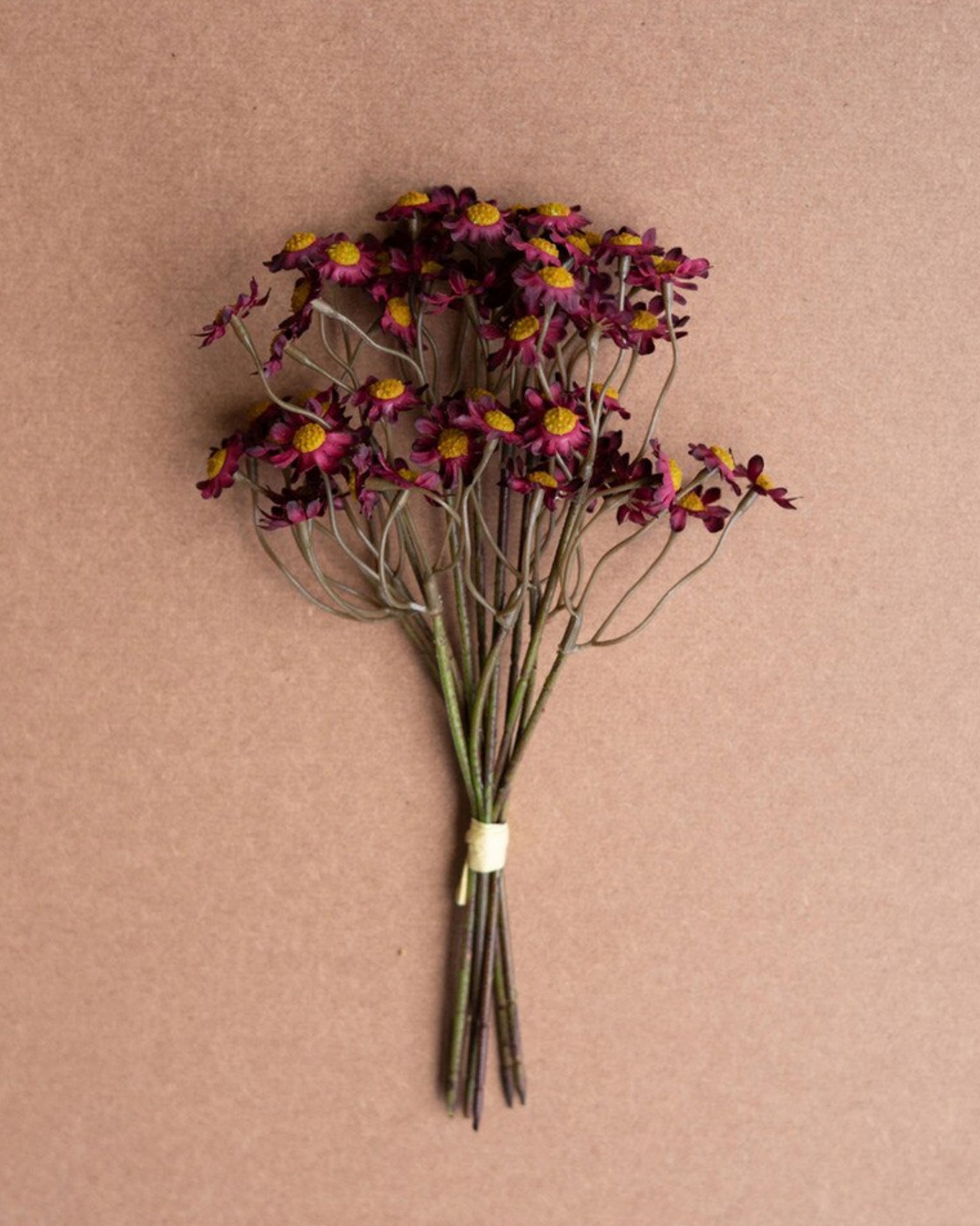 The Kalalou, Inc Faux Chamomile features small dried purple flowers with yellow centers, tied with a light band. Burgundy stems pop against a brown background, making it ideal for cozy fall arrangements.