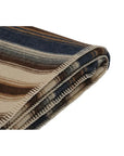 The Faire Cadillac Ranch Throw is a folded wool blanket with stitched edges, featuring horizontal stripes in blue, brown, beige, and cream. It's machine washable for easy care.