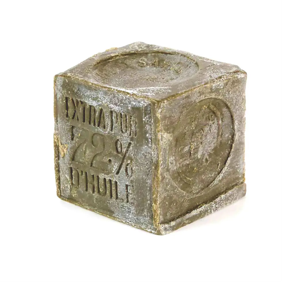 A rectangular, grayish-green Marseille Olive Oil Soap by Cie Luxe Brands features a rough texture and embossed "72%" with Cyrillic text on its surface, displayed against a white background.