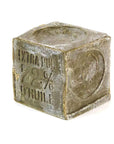 A rectangular, grayish-green Marseille Olive Oil Soap by Cie Luxe Brands features a rough texture and embossed "72%" with Cyrillic text on its surface, displayed against a white background.