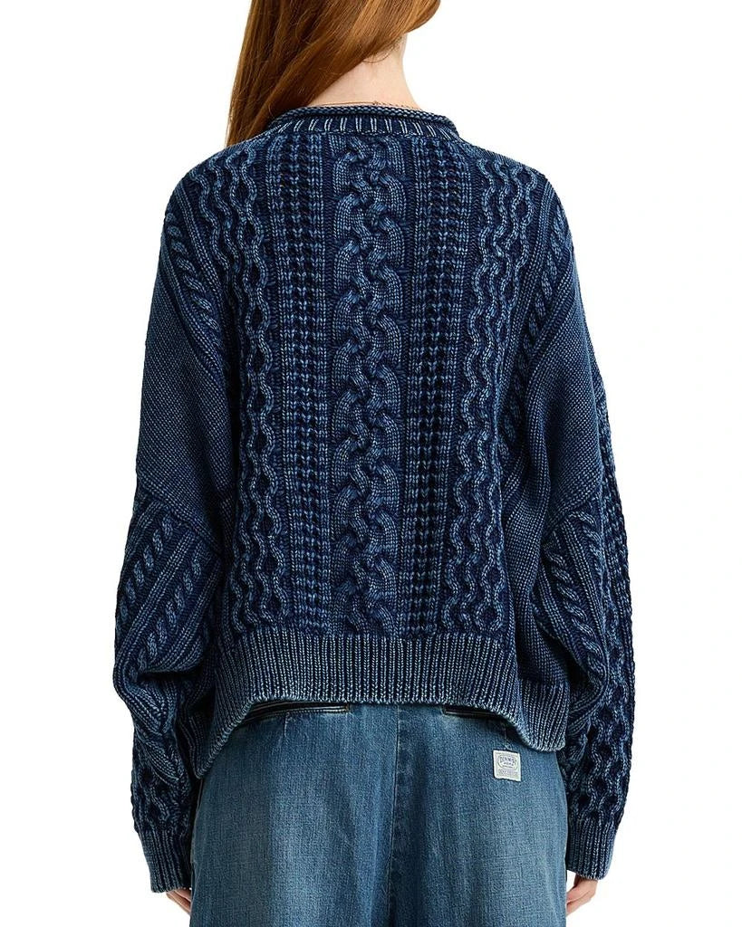 A person with long red hair is seen from the back wearing an oversized Aran sweater with a rolled neck by Denimist and high-waisted denim pants.