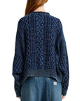 A person with long red hair is seen from the back wearing an oversized Aran sweater with a rolled neck by Denimist and high-waisted denim pants.