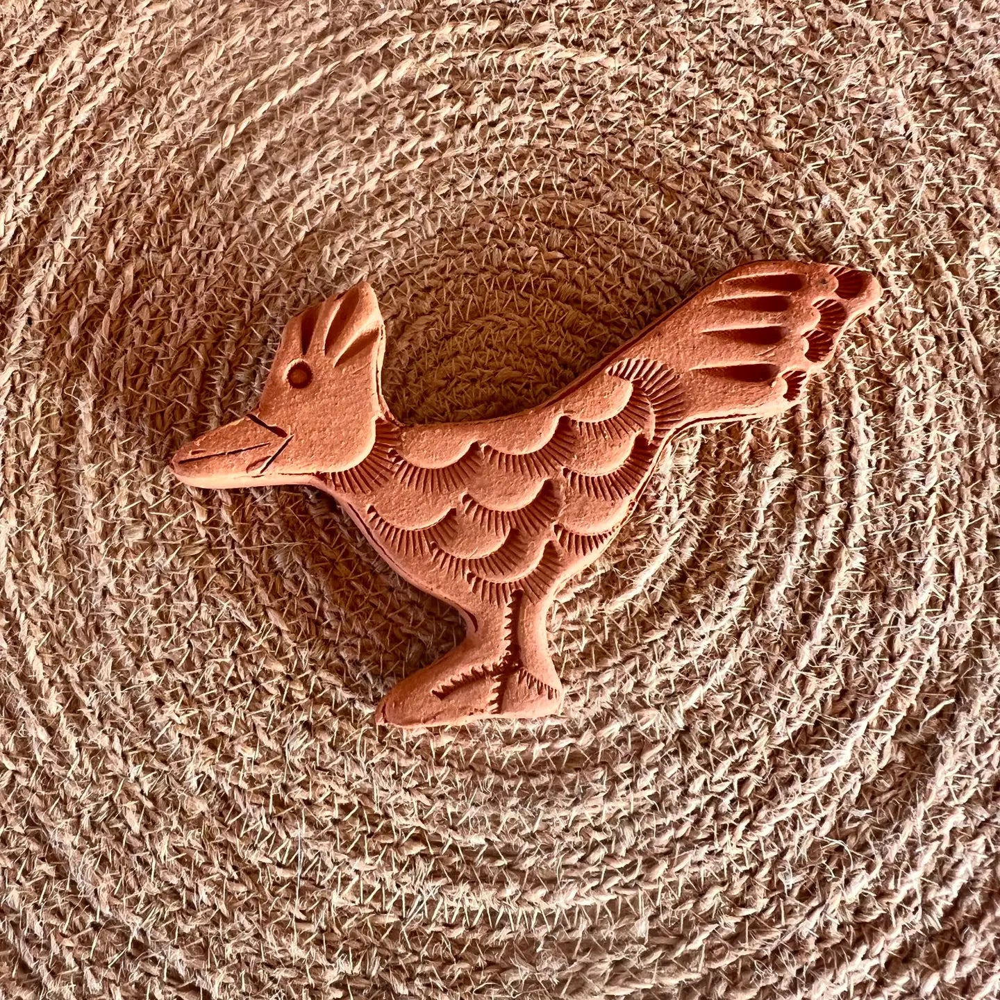 The Faire Brown Sugar Keeper is a handmade, terracotta-colored clay figurine with detailed feather patterns, resting on a woven circular mat, reminiscent of classic ceramic brown sugar keepers.