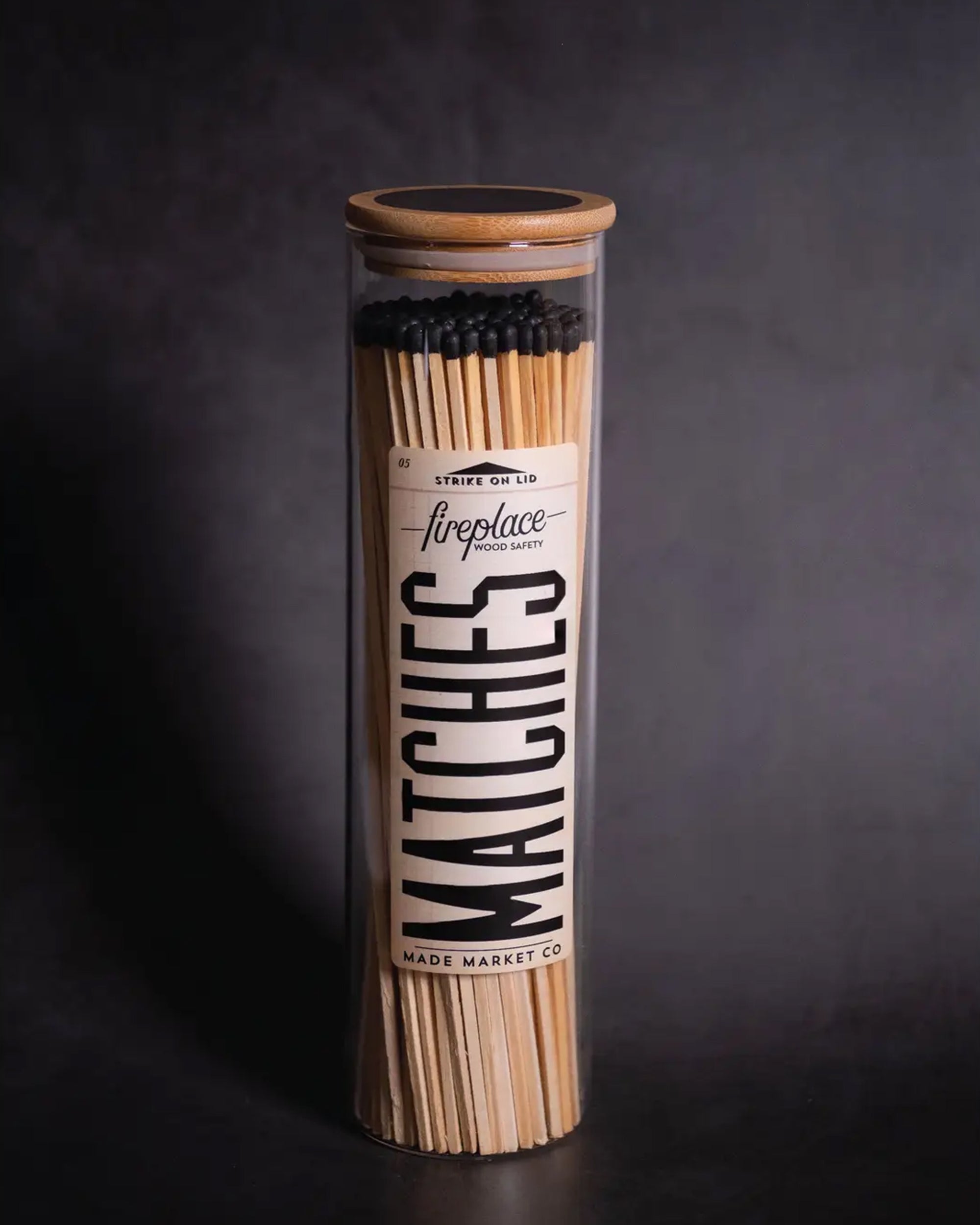 The Fireplaces Apothecary Matches by Faire come in a tall, clear bottle with a wooden lid. Filled with long, black-tipped vintage matches, the bottle features a bold “fireplace MATCHES” label on a dark background for classic appeal.
