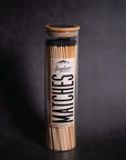 The Fireplaces Apothecary Matches by Faire come in a tall, clear bottle with a wooden lid. Filled with long, black-tipped vintage matches, the bottle features a bold “fireplace MATCHES” label on a dark background for classic appeal.