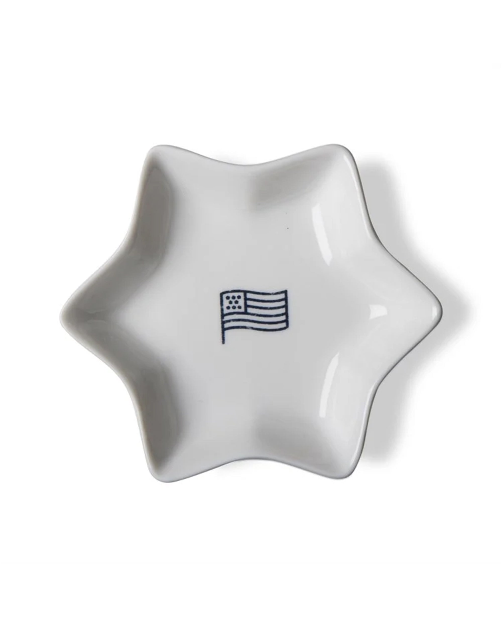 The Tag Flag Star Dish is a white, star-shaped bone china dish with a simple blue American flag outline at the center—an elegant addition to any tableware collection.