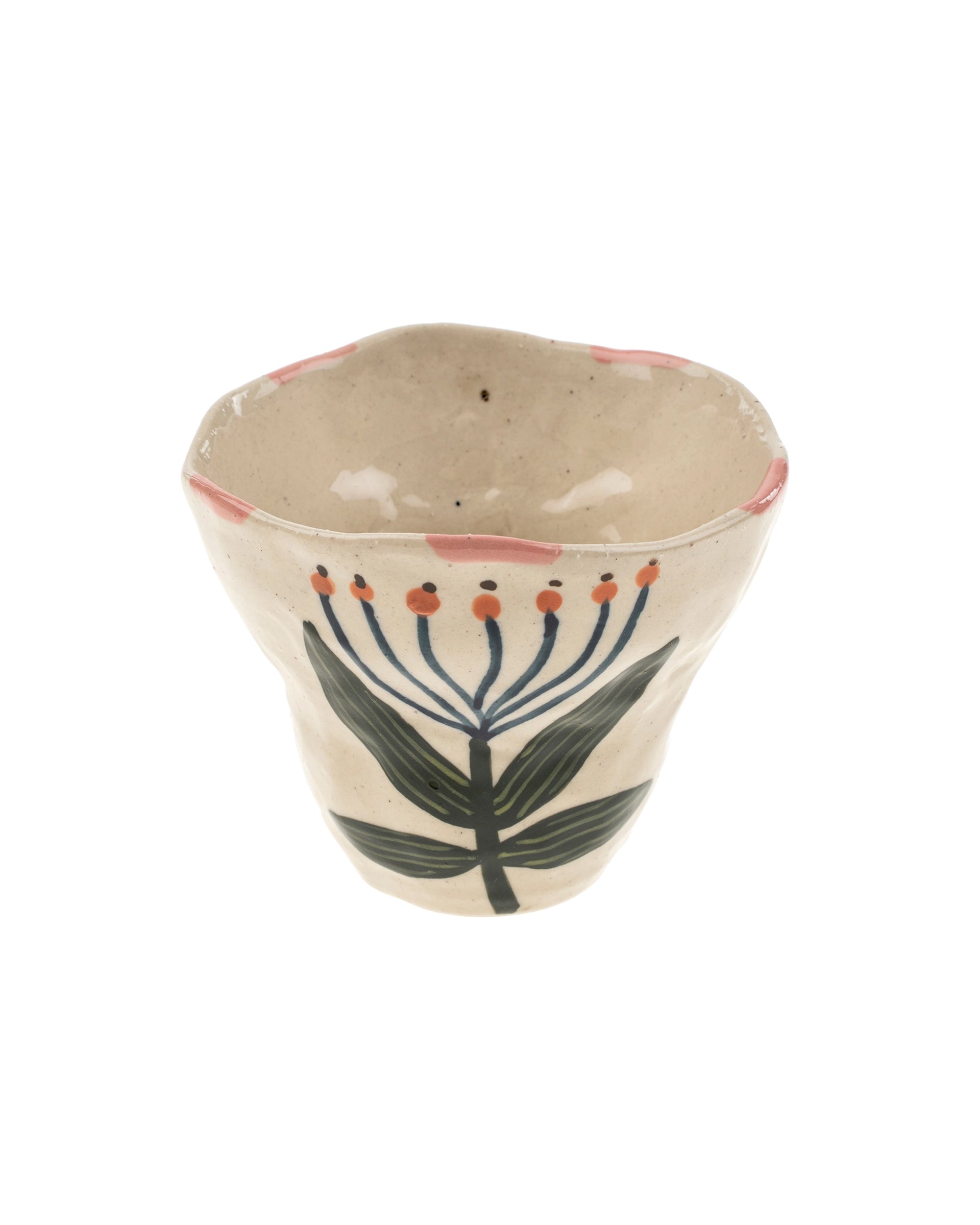 The Flora Pottery Cup by Indaba is a handmade stoneware piece with an uneven rim, featuring hand-painted green leafy plants, blue stems with red dots on a cream background, and pink accents—a unique artisan creation.