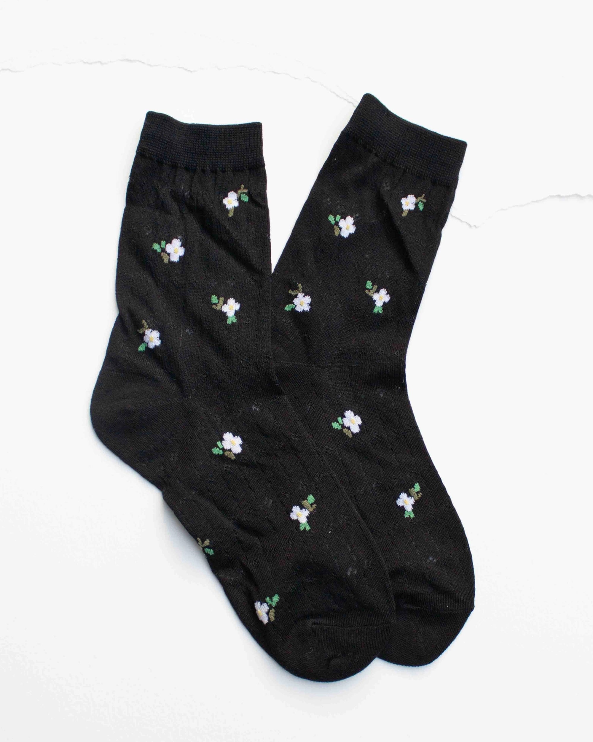 Faire Mini Floral Cotton Socks in black, featuring white and purple flowers with green leaves, are laid flat on a white background. Made from breathable cotton, these feminine socks offer all-day comfort.
