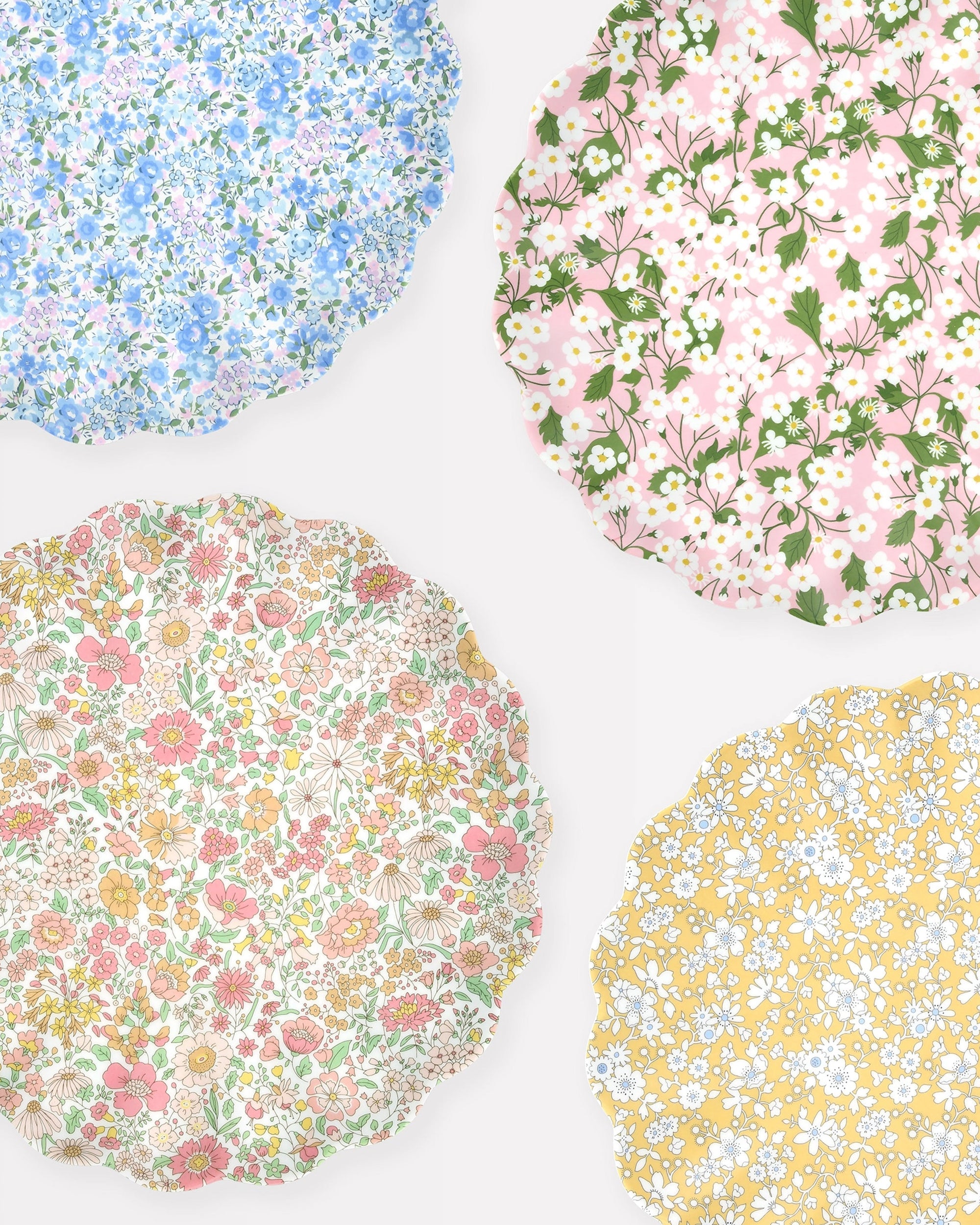 The Faire Mixed Set Reusable Large Plates features four scallop plates with floral patterns—blue, pink, yellow, and multicolor—on light backgrounds. Perfect decorative party plates for any cheerful gathering.