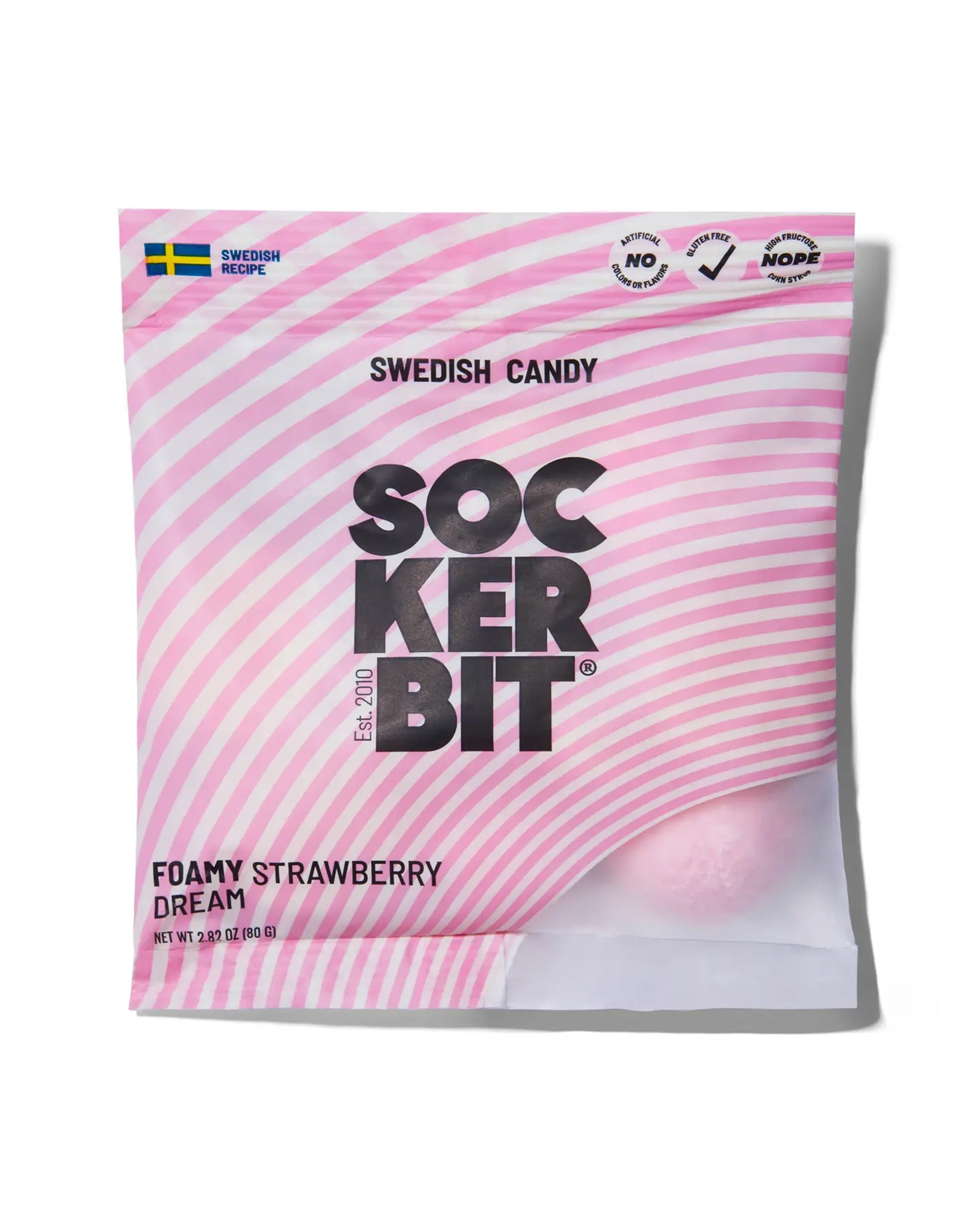 A pink and white striped Faire "Foamy Strawberry Dream" bag of non-GMO Swedish candy features a small window revealing a pink foamy strawberry bite, the Swedish flag, and product details on the packaging.