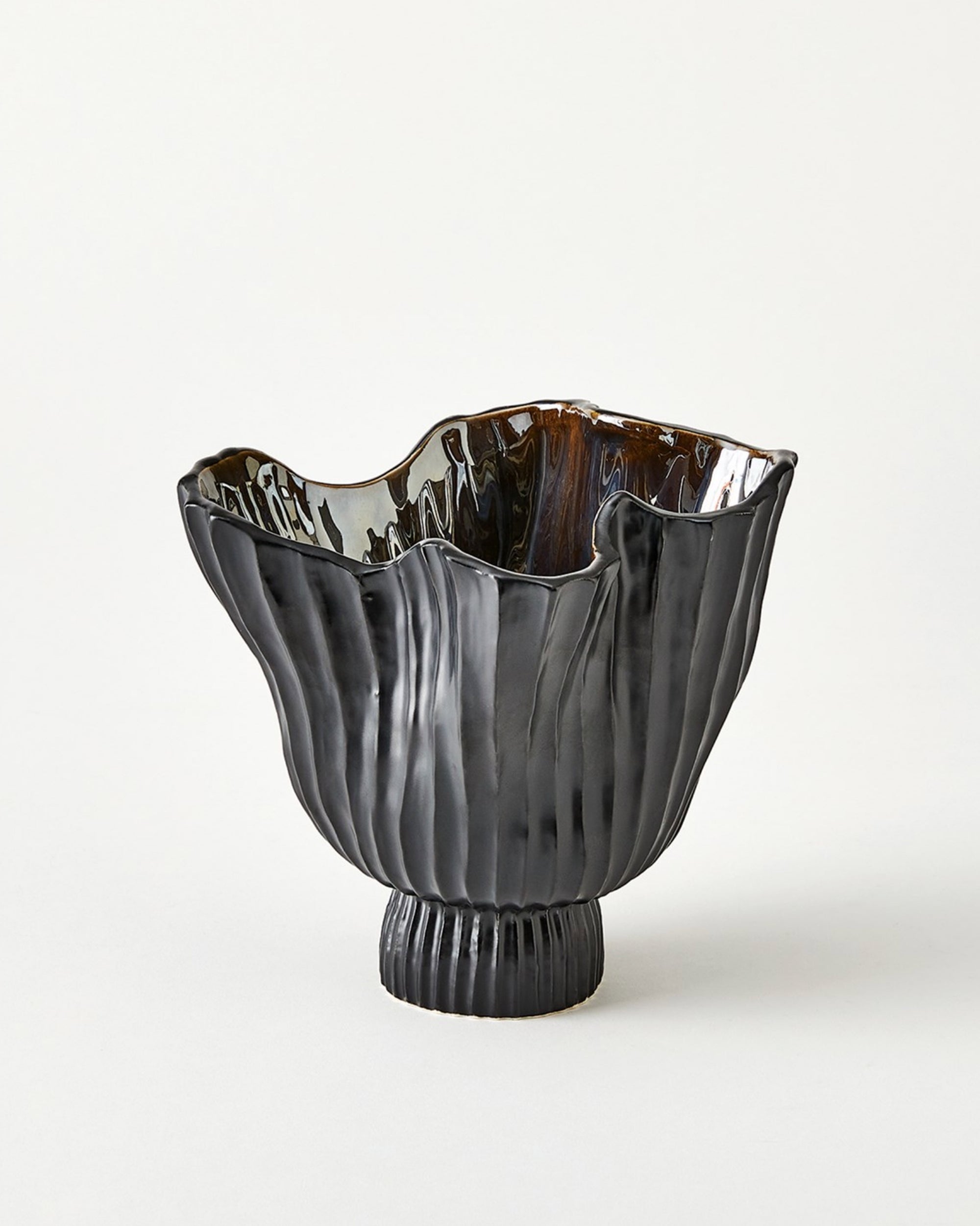 The 7.10753 Folha Footed Vase S by Global Views is a glossy black ceramic vase with an irregular wavy rim, vertical textured lines, a ribbed base, and a hand-painted metallic interior crafted by Portuguese artisans.