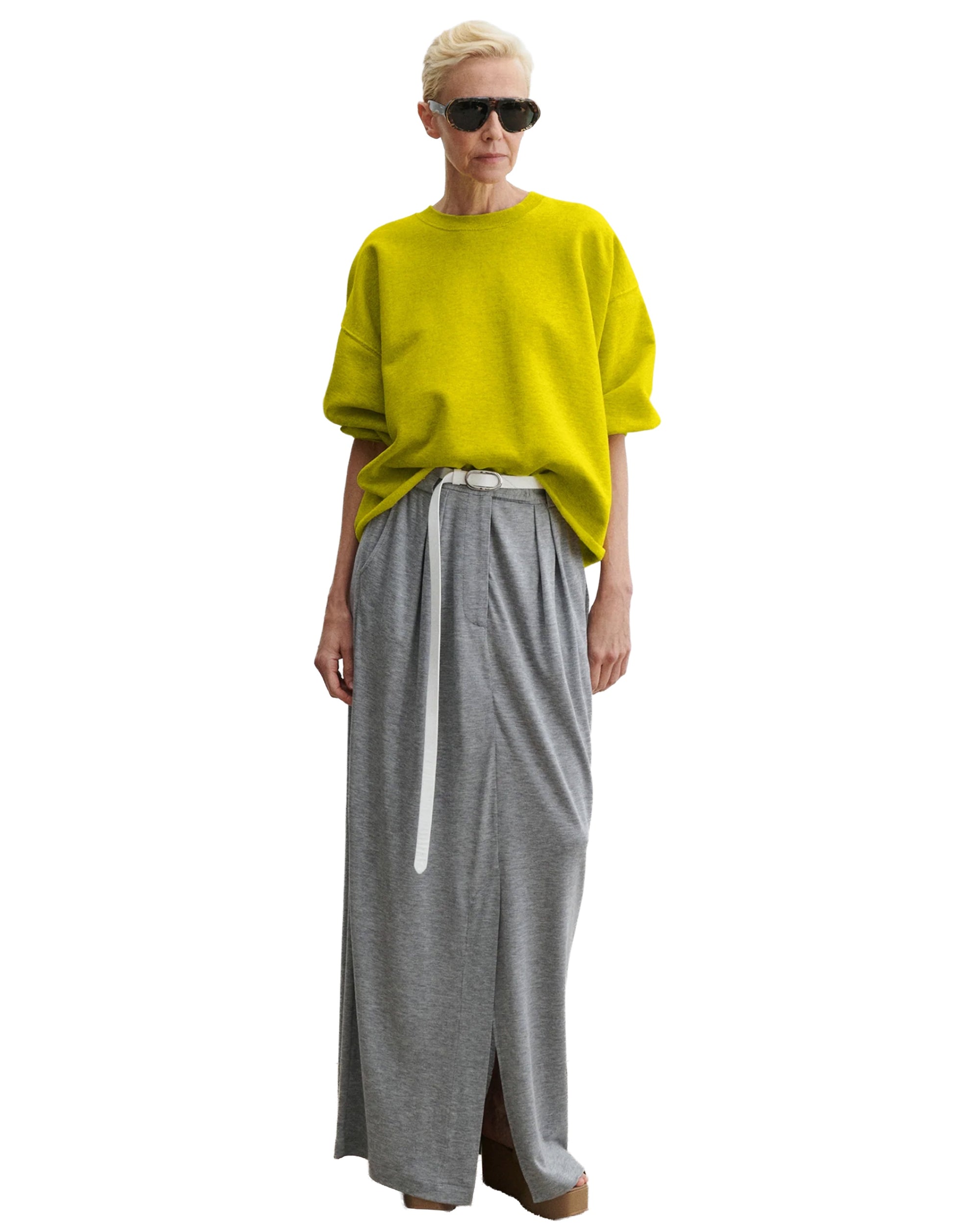 Wearing the Rachel Comey Fond Sweatshirt in bright yellow, a person pairs it with a gray maxi skirt with a front slit, white belt, brown shoes, and black sunglasses, standing against a white background.