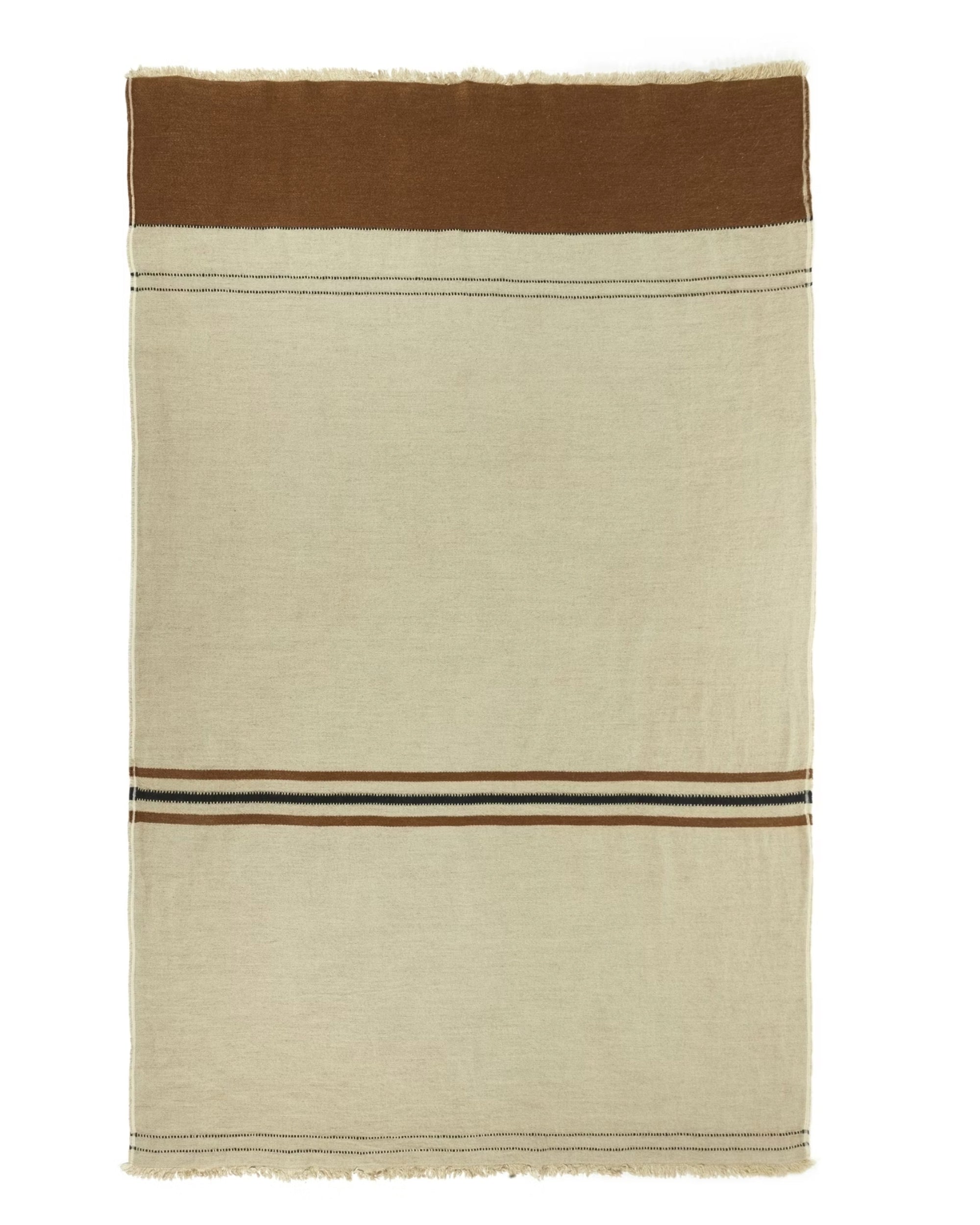 The Libeco Home Foundry Throw is a rectangular beige stonewashed blanket with a wide brown top band, thin black and brown stripes near the lower third, and fringed edges.