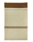 The Libeco Home Foundry Throw is a rectangular beige stonewashed blanket with a wide brown top band, thin black and brown stripes near the lower third, and fringed edges.
