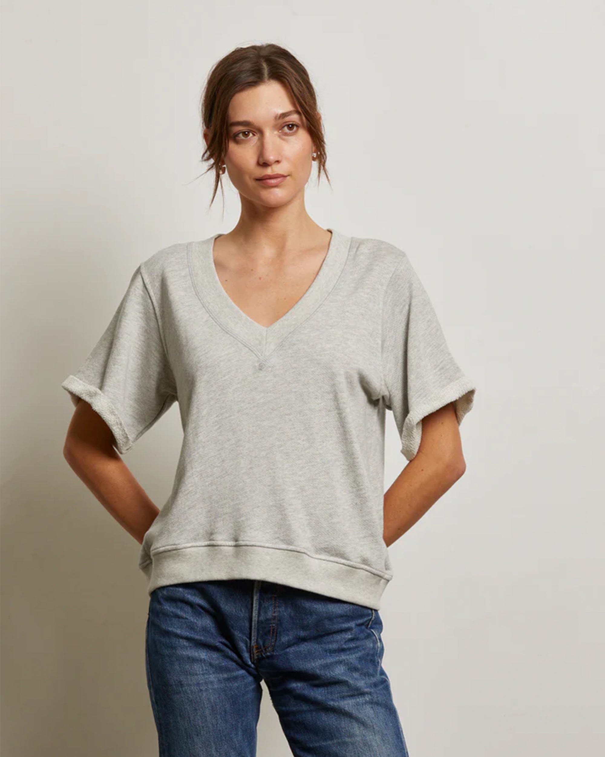 A woman wearing a Perfectwhitetee French Terry SS Crew in light gray and blue jeans stands against a plain, light-colored background with her hands behind her back.