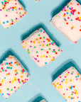 Faire Funfetti Marshmallows—colorful, allergy-friendly squares with rainbow sprinkles—are evenly spaced on a light blue background in a playful diagonal pattern.