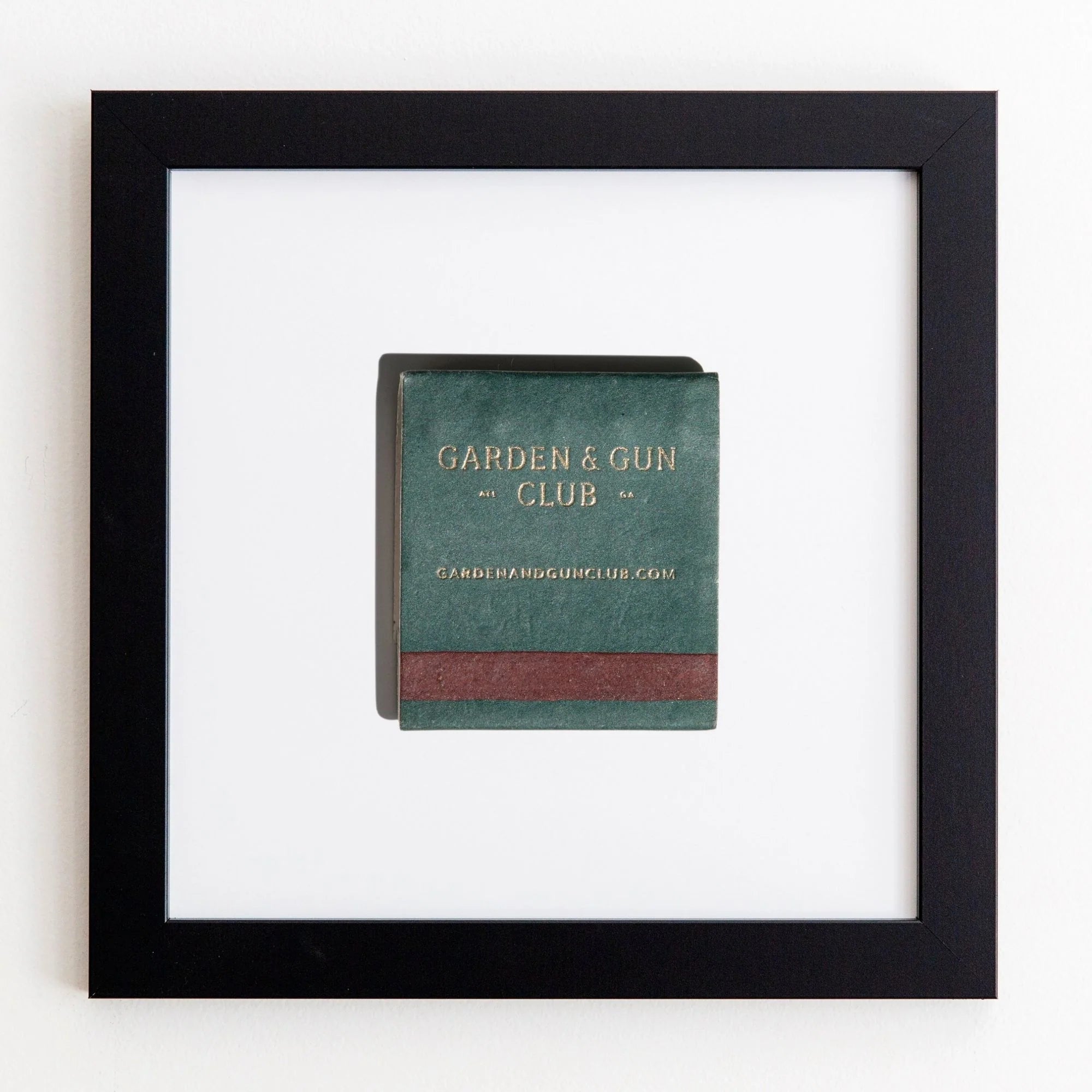 A framed book titled &quot;GARDEN &amp; GUN CLUB&quot; displayed on a white wall. The book cover is dark green with a red spine, and the title is in uppercase letters with Match South Art Square Black Frames.