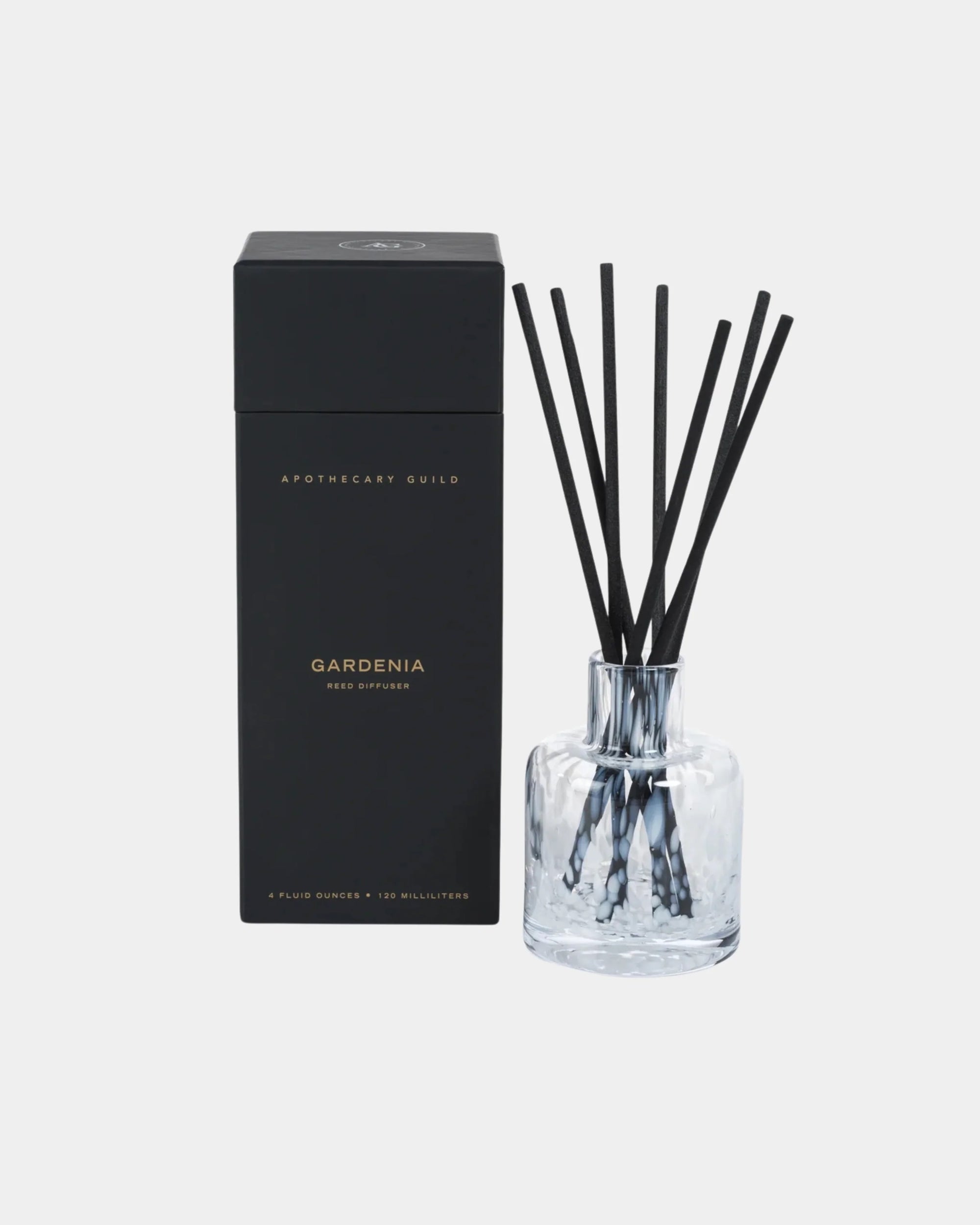The Zodax CH-7294 Diffuser Gardenia features a clear glass vessel with black reeds and a tall black box, offering an elegant, minimalist design to enhance your home&#39;s aroma against a white backdrop.